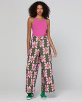 Woman wearing a pink sleeveless top and green pants with floral pattern on a white background