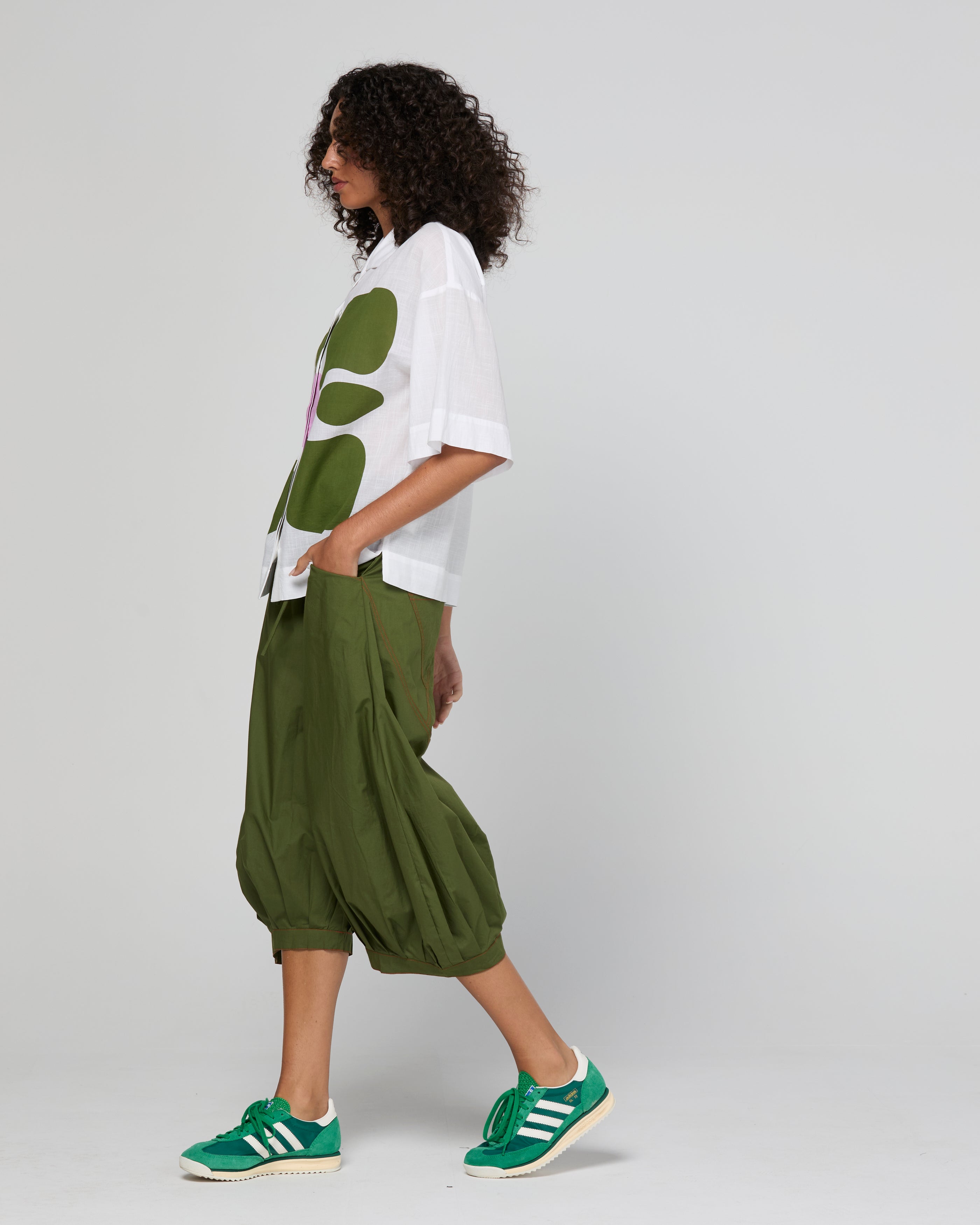 Woman wearing a white shirt with green leaf patterns and green pants on a gray background