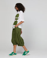 Woman wearing a white shirt with green leaf patterns and green pants on a gray background
