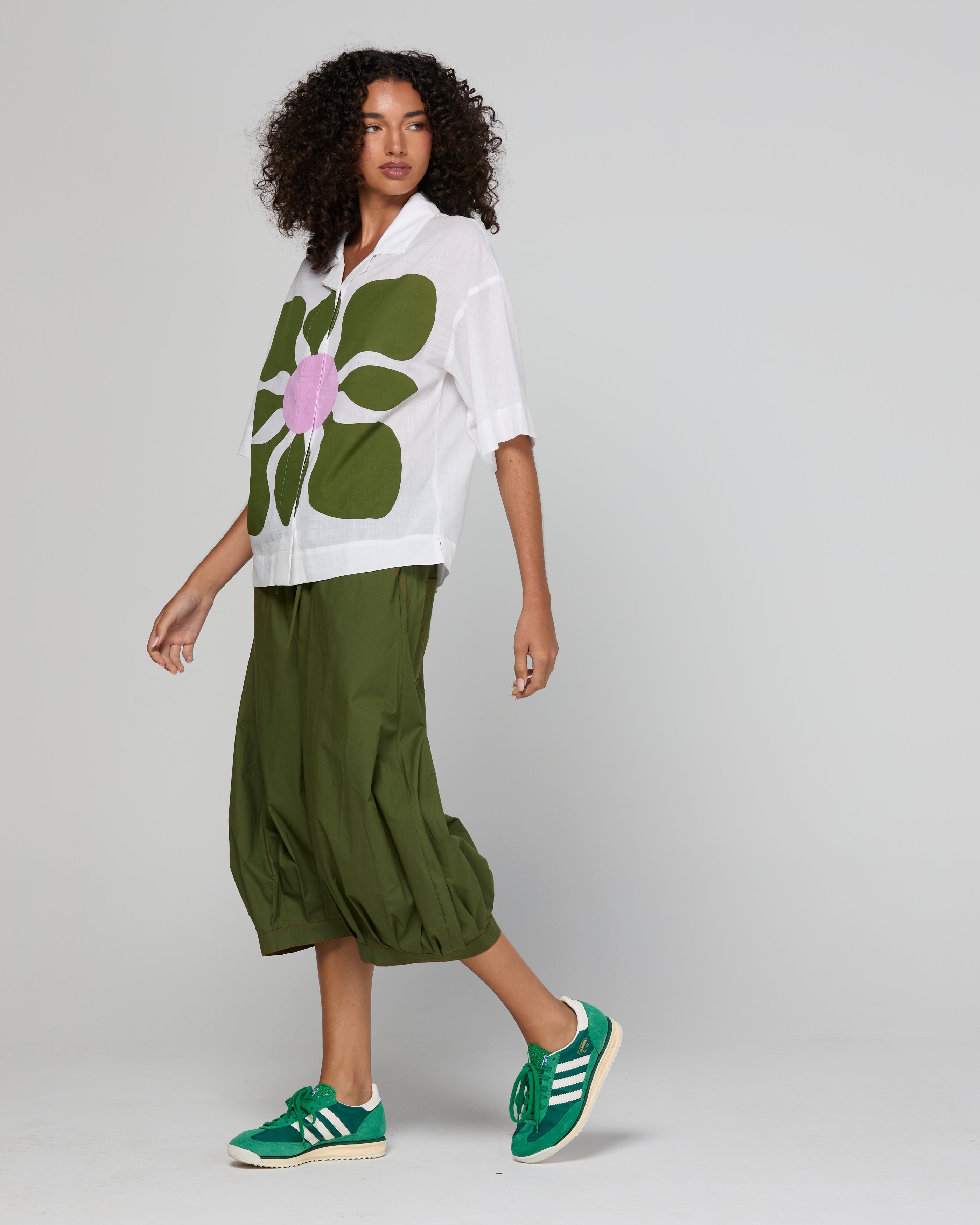 Woman wearing a white shirt with a green floral design, green pants, and green sneakers on a light gray background