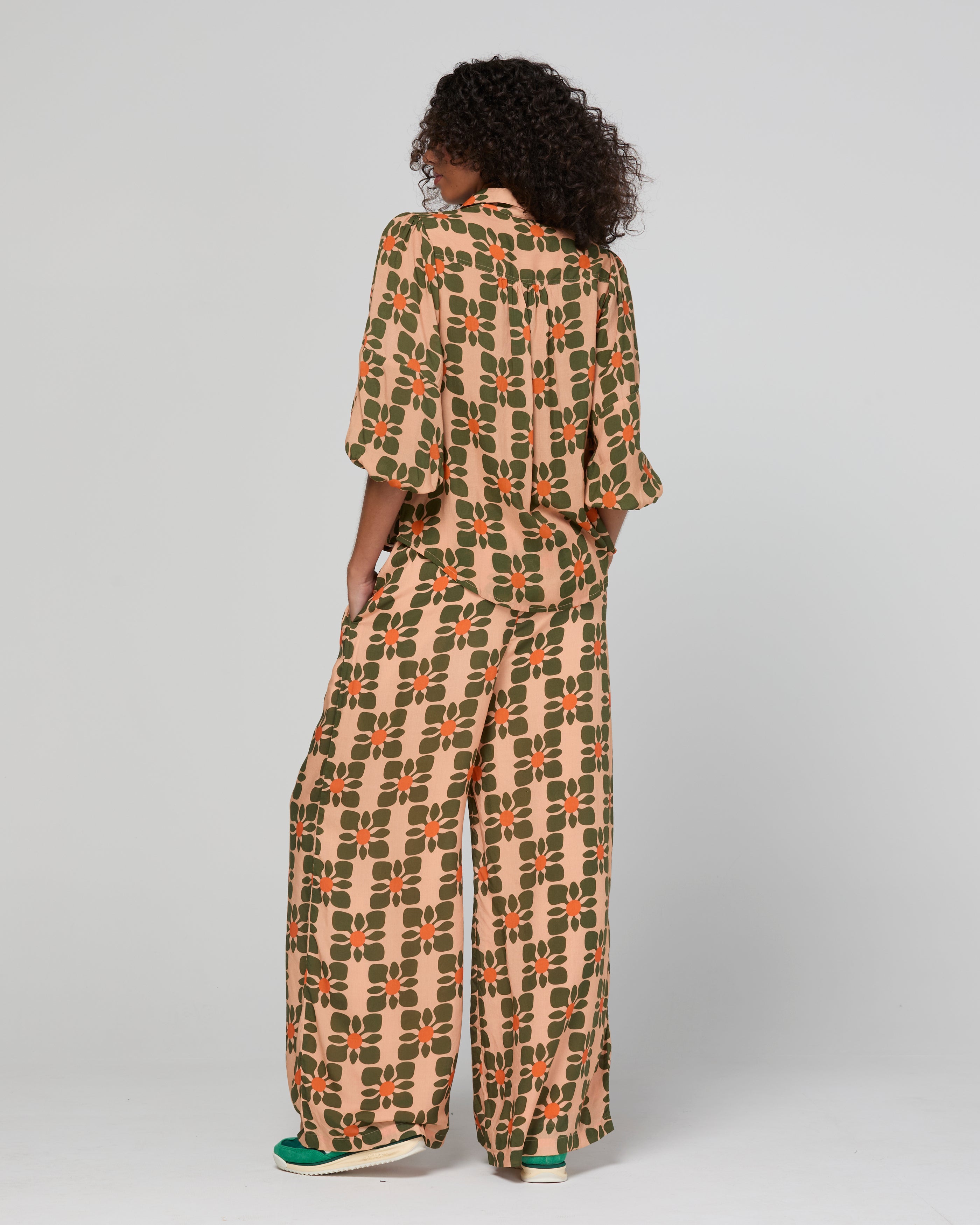 Lady wearing a orange floral patterned outfit on a plain background