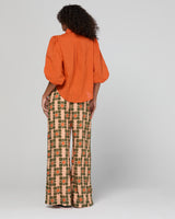 Person wearing an orange blouse and patterned pants on a plain background