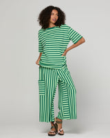A model wearing a green and white striped two-piece lounge set, featuring a short-sleeve top and wide-leg pants with cargo pockets, styled with brown sandals.