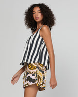 A woman modeling a sleeveless top and shorts set against a plain light gray studio background. The top has vertical black and white stripes, while the shorts feature a multicolor paisley and floral pattern in yellow, brown, black, and white.