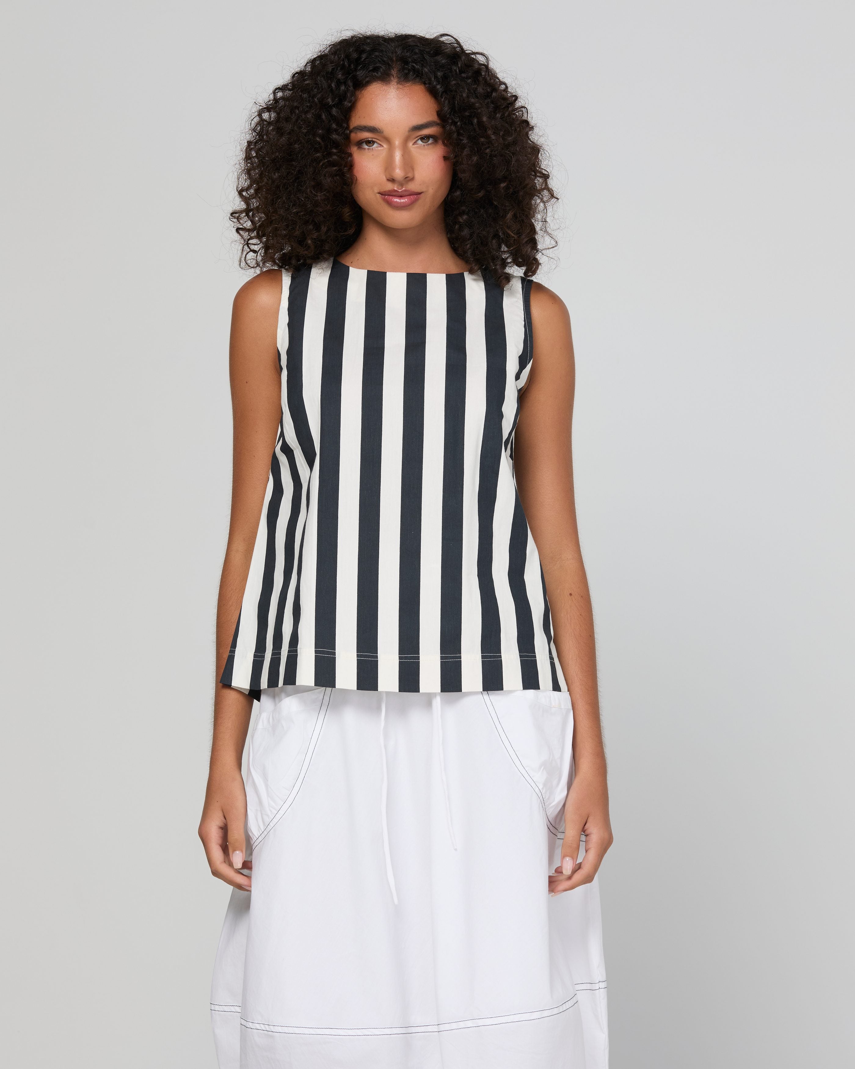 A model wearing a sleeveless top with vertical black and white stripes, paired with a white skirt, against a light gray studio background.