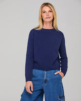 Woman wearing a navy blue jumper and blue jeans against a gray background