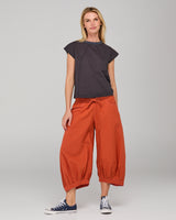 Woman wearing a slate cotton top and orange guru pants on a gray background