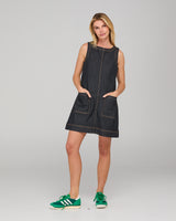 Woman wearing a dark denim tunic dress with green sneakers on a gray background