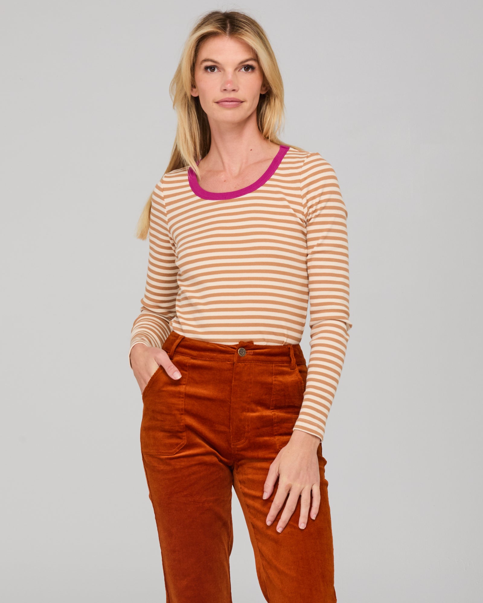 lady wearing a cream and white striped shirt and rust corduroy pants on a gray background