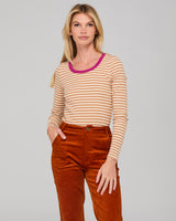 lady wearing a cream and white striped shirt and rust corduroy pants on a gray background