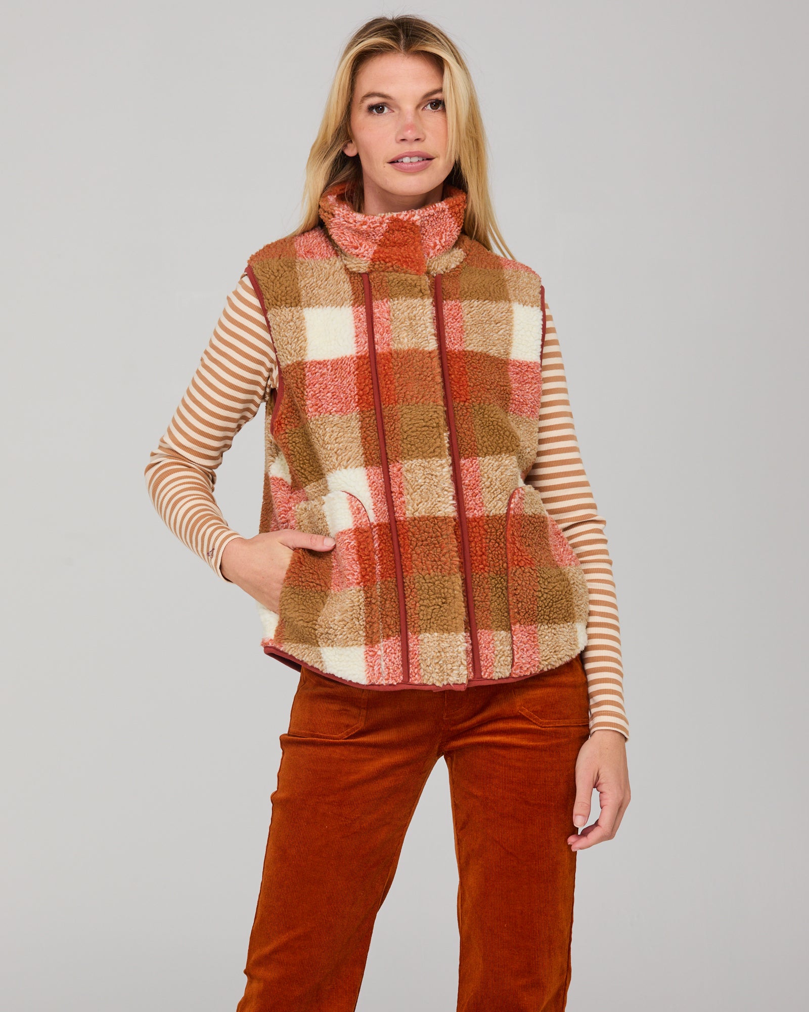 Woman wearing a red and brown plaid fleece vest over a striped shirt with rust corduroy pants 