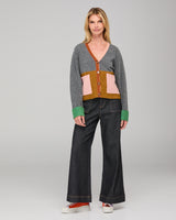 Woman wearing a grey patterned cardigan and dark denim jeans on a gray background