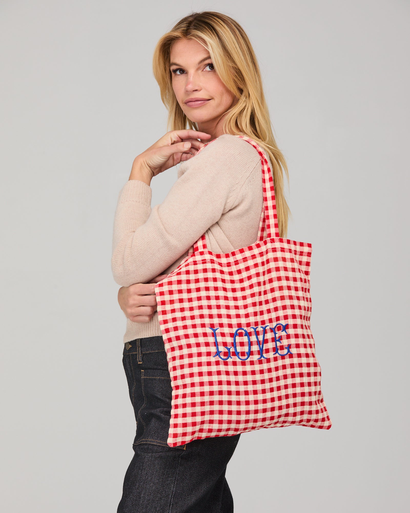 Woman holding a red and white checkered tote bag with 'LOVE' embroidery on a gray background
