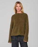 Woman wearing a khaki green sweater and dark denim jeans on a gray background