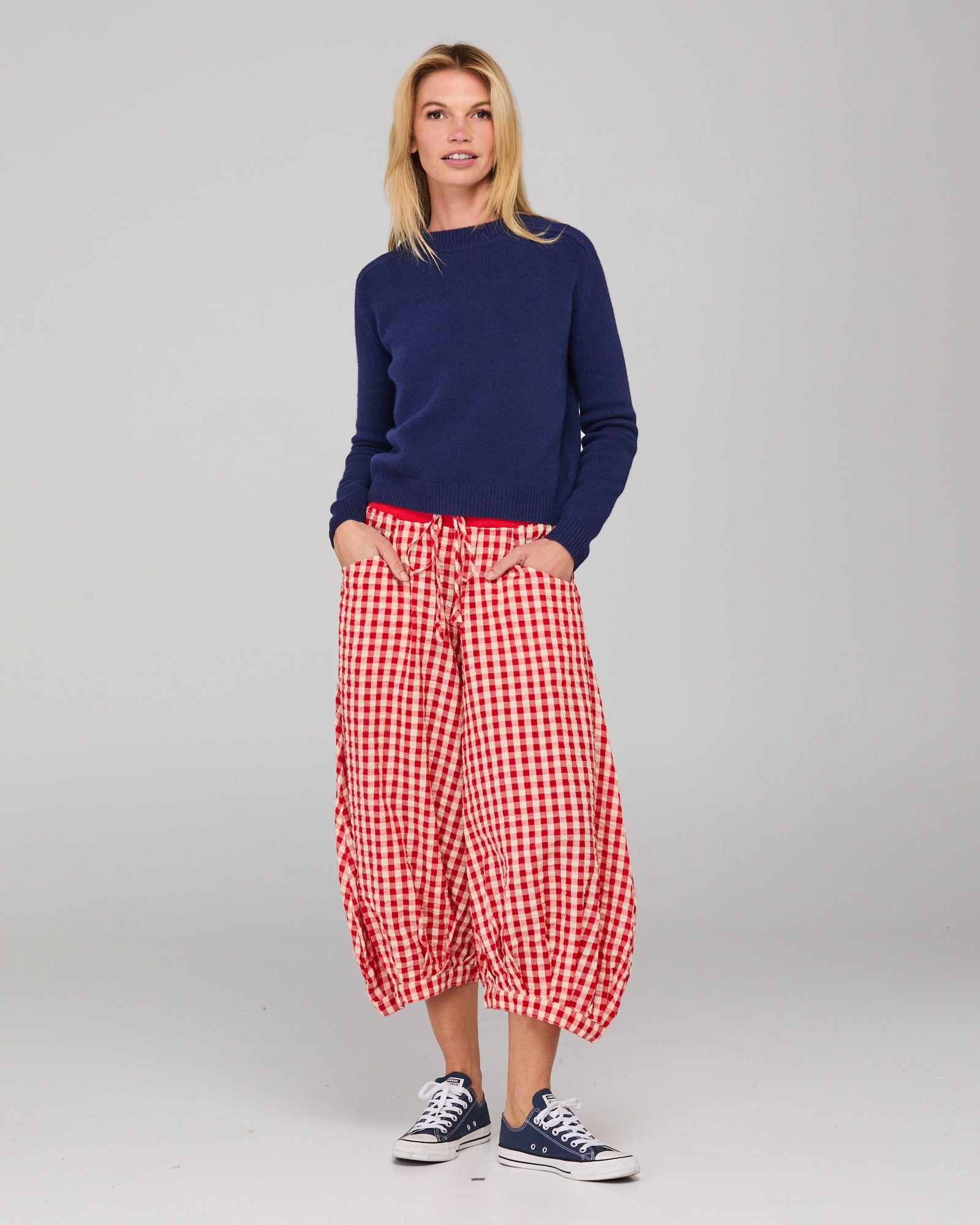 Woman wearing a navy jumper and red and white checkered pants on a gray background