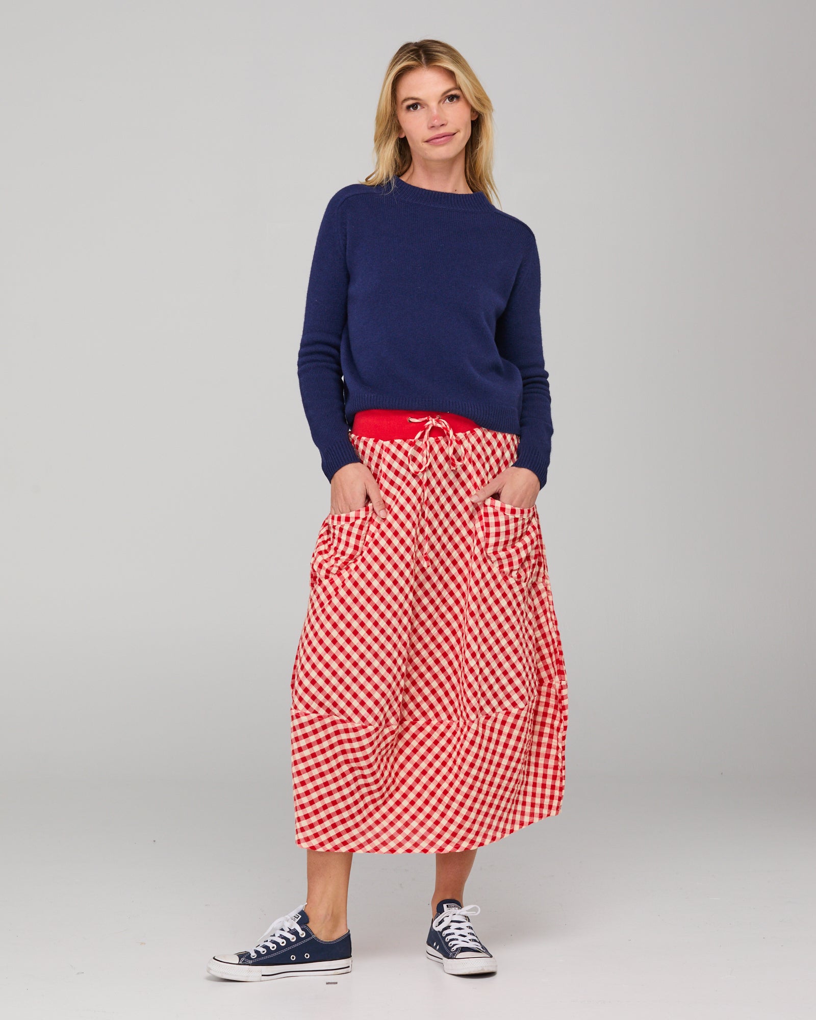 Woman wearing a navy sweater and red checkered skirt on a gray background