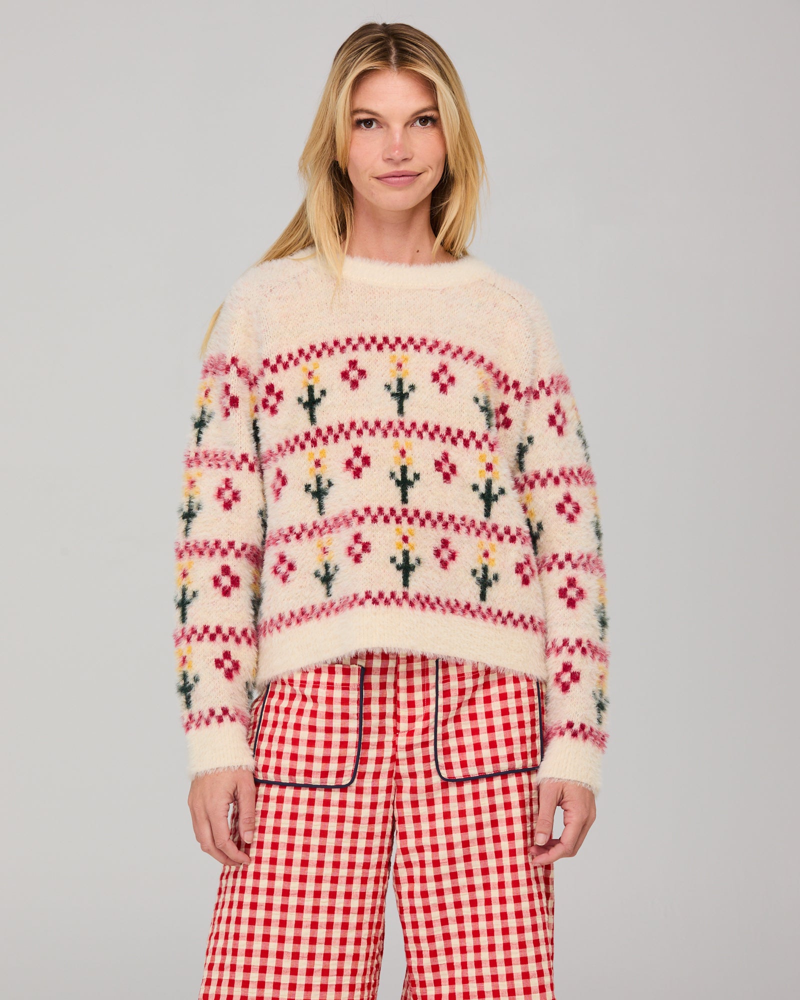 Woman wearing a cream patterned jumper and red gingham pants on a gray background