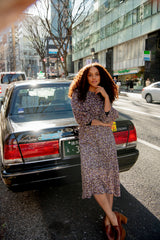 Woman in a patterned dress standing on a city street with a taxi in the background