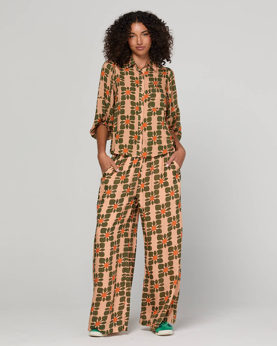 Woman wearing a orange patterned shirt and pants on a plain background