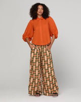 Woman wearing an orange blouse and patterned pants on a white background