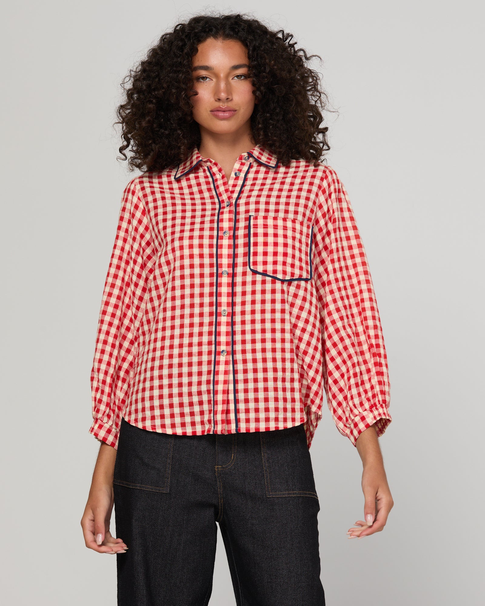 Woman wearing a red and white gingham checkered shirt with navy trim against a gray background