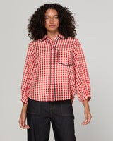 Woman wearing a red and white gingham checkered shirt with navy trim against a gray background
