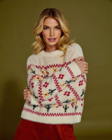Woman wearing a cream red and yellow flower patterned sweater against a solid background